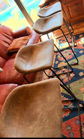 Modern set of 4 bar stools has brown faux leather upholstered seats.