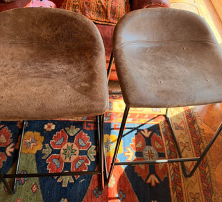 Modern set of 4 bar stools has brown faux leather upholstered seats.