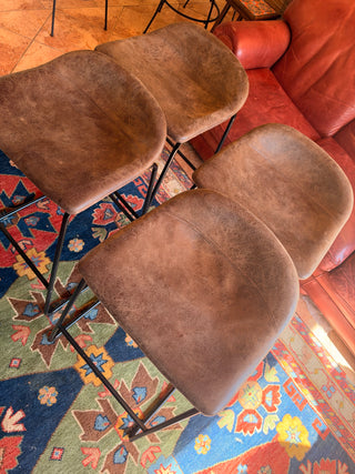 Modern set of 4 bar stools has brown faux leather upholstered seats.
