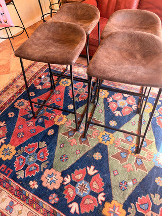 Modern set of 4 bar stools has brown faux leather upholstered seats.
