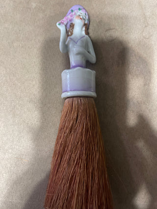 large whisk  broom, woman with purple hat, and dress