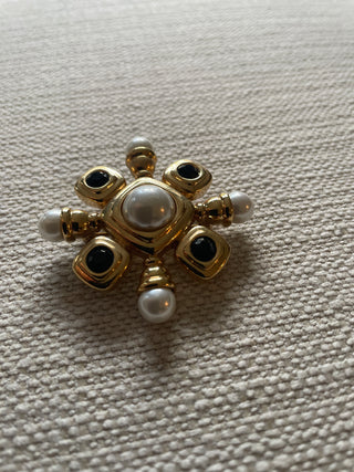 vintage St. John gold-tone brooch features black cabochons and faux pearls arranged in a starburst or Maltese cross design.